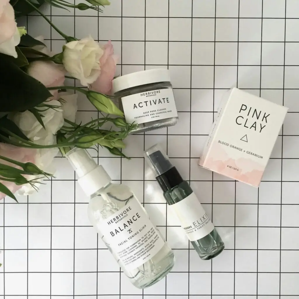 A flat lay of Herbivore Botanicals products with natural elements like flowers and leaves