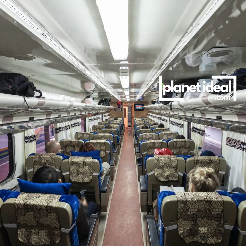 A train interior with spacious seating, sunlight pouring in through large windows, and passengers enjoying the ride.
